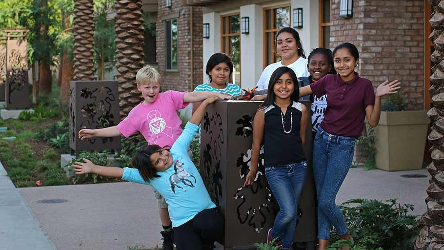 Happy children who live at Rockwood in Anaheim, CA stand around monument sign