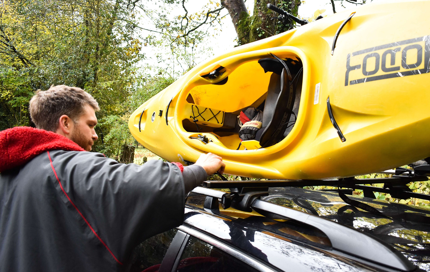 A Kayak On Top Of A Car Being Removed By A Man With The Red Original Change Jacket On