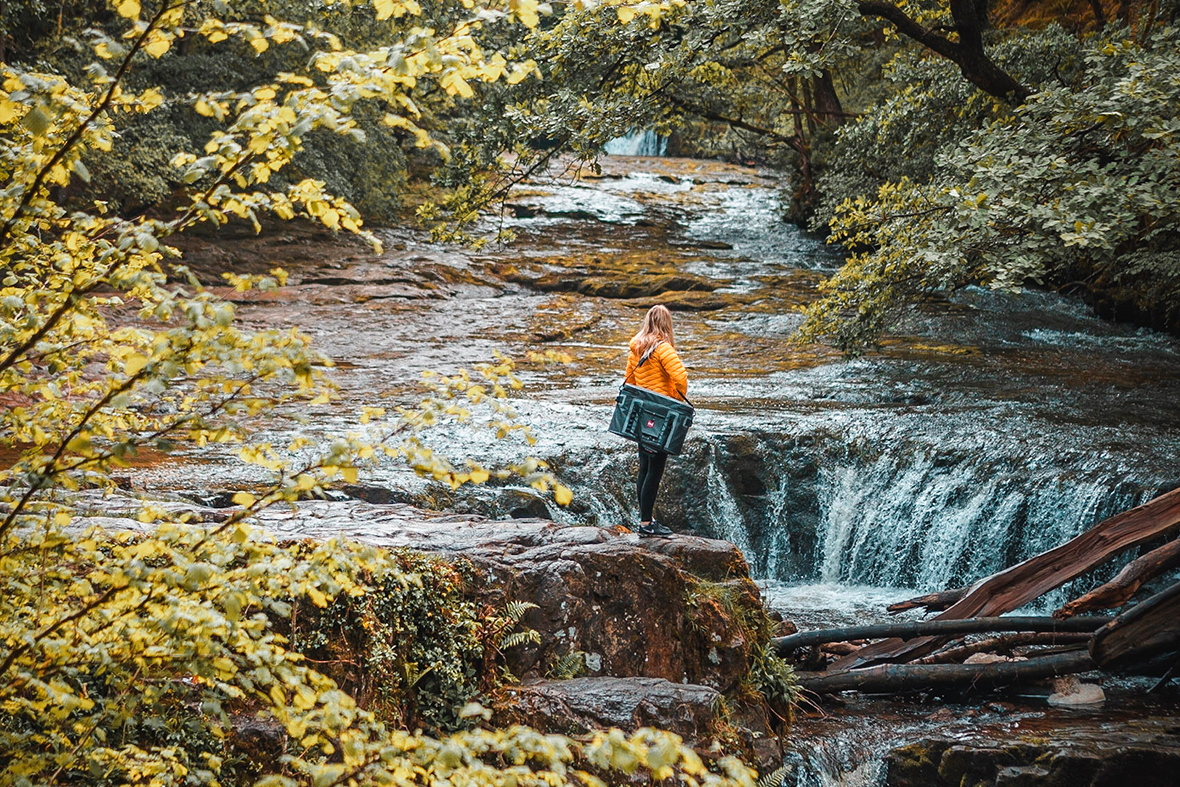 Female carries cool bag along river.