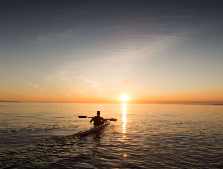 A Man Kayaking Out Into The Sunset