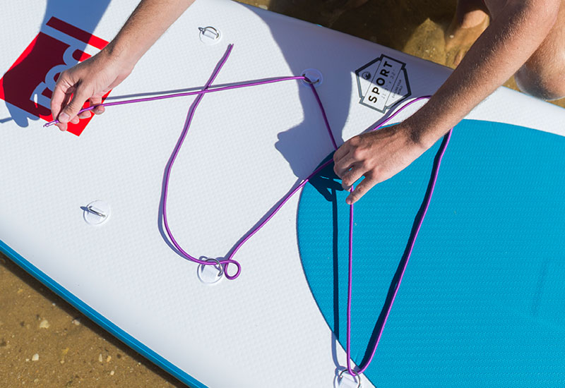 threading the Red Original Purple Cargo Bungee through the cargo points on a SUP