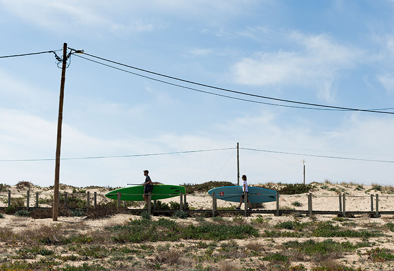 people carrying paddle boards in sand dunes