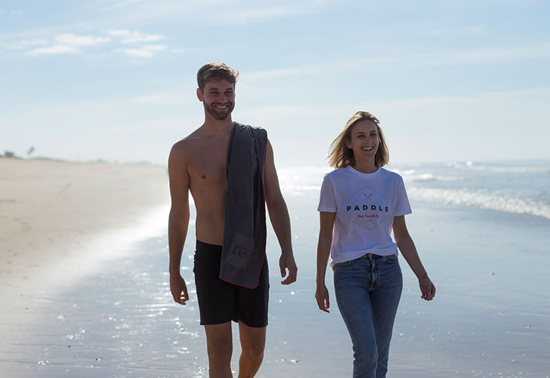 Coupe walking on the beach with the woman wearing the Red Original paddle on t-shirt